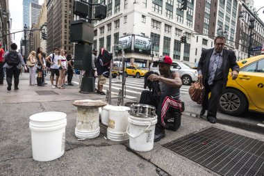 New York City, USA - July 25, 2018: Drummer man playing from plastic pots like a drum on Seventh Avenue (7th Avenue) while a man in a suit comes out of a taxi and people around in Manhattan in New York City, USA clipart