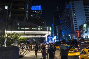 New York City, USA - July 30, 2018: Sheraton New York Times Square Hotel at night on Seventh Avenue (7th Avenue) next to Times Square with people around and a bellboy in Manhattan in New York City, USA clipart