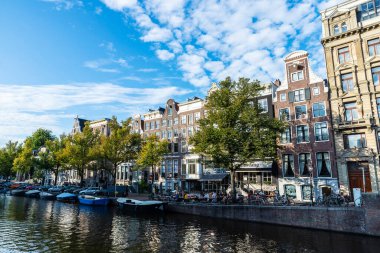 Amsterdam, Hollanda - 9 Eylül 2018: Amsterdam, Hollanda 'da bar teraslarında insanların bulunduğu bir kanal boyunca eski geleneksel eğimli evler