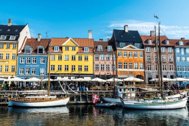Kopenhag, Danimarka - 27 Ağustos 2019: Teras barında içki içen insanlar ve Nyhavn, Kopenhag, Danimarka 'da bir kanalda demirlemiş eski ahşap yelkenliler 