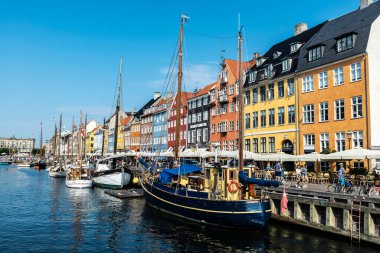 Kopenhag, Danimarka - 27 Ağustos 2019: Teras barında içki içen insanlar ve Nyhavn, Kopenhag, Danimarka 'da bir kanalda demirlemiş eski ahşap yelkenliler 