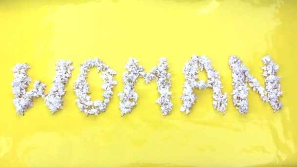 De inscriptie Woman is geschreven in witte bloemen van lila op een gele achtergrond. Het woord Vrouw is geschreven met lila bloemen. Bloeminscriptie Vrouw. — Stockvideo