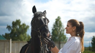 Beyaz gömlekli bir kız, sıcak ve güneşli bir havada sokakta bir atı kollarından besliyor.