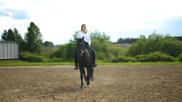 Dívka v bílé košili a černé kalhoty jezdí na koni — Stock fotografie