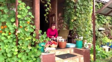 Kadın çiçekler boğulma güzel bir kır evinin verandasında iki sepet ile oturur.