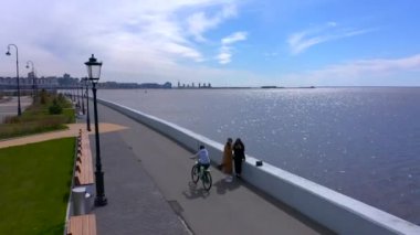 PETERSBURG, RUSSIA - 22 Mayıs 2020: gri ceketli ve siyah pantolonlu bir bisikletçi gezinti güvertesinde geziniyor. Şehrin üzerinde İHA uçuşu.