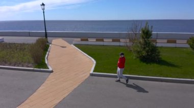 PETERSBURG, RUSSIA - 22 Mayıs 2020: kırmızı kazaklı bir adam akıllı telefonla konuşuyor ve gezinti güvertesi boyunca yürüyor. Şehrin üzerinde İHA uçuşu.