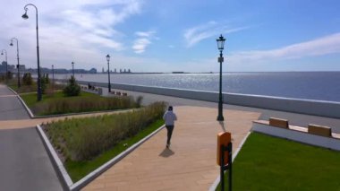 PETERSBURG, RUSSIA - 22 Mayıs 2020: gri kazaklı bir kız gezinti güvertesi boyunca koşuyor. Şehrin üzerinde İHA uçuşu.
