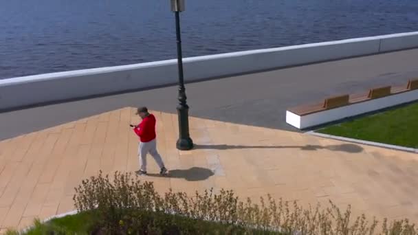 2020年5月22日 赤いセーターの男がスマートフォンで話していて 遊歩道を歩いている 街を飛行中 — ストック動画