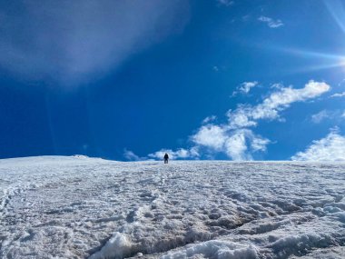 Sırt çantası ve yürüyüş direkleri olan bir dağcı karlı bir buz patikasında duruyor. Kuzey Elbrus bölgesinin karlı yamaçları. Güzel dağ kış manzarası.