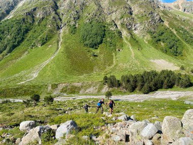 Üç dağcı bir dağ yolu boyunca gider. Güzel bir dağ manzarasının havadan görünüşü. Kuzey Elbrus bölgesinin yeşil kayalık yamaçları.