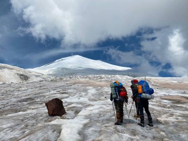 Elbrus Dağı. Sırt çantaları ve yürüyüş direkleriyle üç dağcı karlı bir buz dağının üzerinde duruyor. Kuzey Elbrus bölgesinin karlı yamaçları. Güzel dağ kış manzarası.