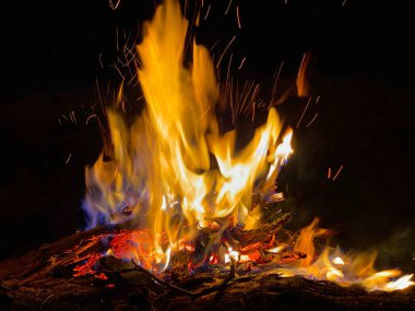 Geceleri ormanın önünde kıvılcımlar ve partiküllerle yanan büyük bir şenlik ateşi..