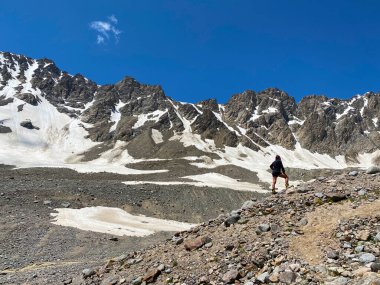 Bir dağcı bir dağ yolunda duruyor ve uzaklığa bakıyor. Güzel bir dağ kış manzarasının havadan görünüşü. Kuzey Elbrus bölgesinin kayalık yamaçları.