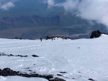 Elbrus Dağı. Sırt çantalı ve sırıklı tırmanışçılar karlı bir patika boyunca yürürler. Güzel dağ kış manzarası. Kuzey Elbrus bölgesinin karlı yamaçları.