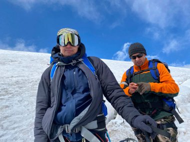 Sırt çantaları ve yürüyüş direkleri olan iki dağcı kar yolunda duruyor. Kuzey Elbrus bölgesinin karlı yamaçları. Dağ kış manzarası.