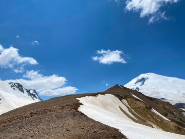 Güzel bir kış dağ manzarasının havadan görünüşü. Kuzey Elbrus bölgesinin kayalık yamaçları. Beyaz bulutlu mavi gökyüzü