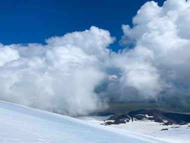 Güzel bir kış dağ manzarasının havadan görünüşü. Kuzey Elbrus bölgesinin kayalık yamaçları. Beyaz bulutlu mavi gökyüzü.