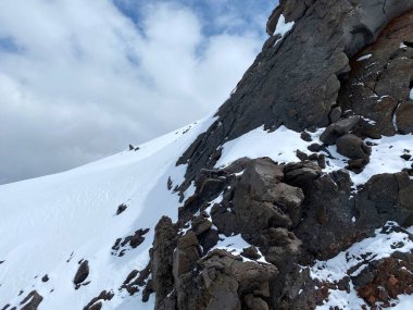 Güzel bir kış dağ manzarasının havadan görünüşü. Kuzey Elbrus bölgesinin kayalık yamaçları. Beyaz bulutlu mavi gökyüzü.