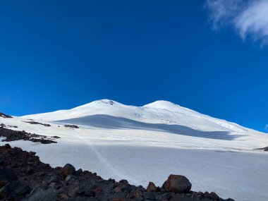 Elbrus Dağı. Güzel bir kış dağ manzarasının havadan görünüşü. Kuzey Elbrus bölgesinin kayalık yamaçları. Beyaz bulutlu mavi gökyüzü.