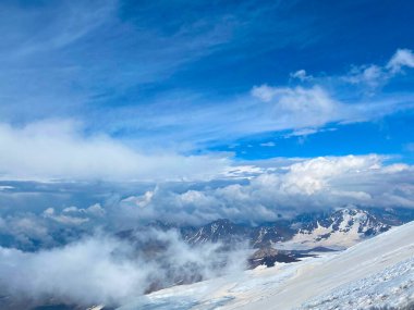 Elbrus Dağı 'nın yüksekliğinden bak. Güzel bir kış dağ manzarasının havadan görünüşü. Kuzey Elbrus bölgesinin kayalık yamaçları. Beyaz bulutlu mavi gökyüzü.