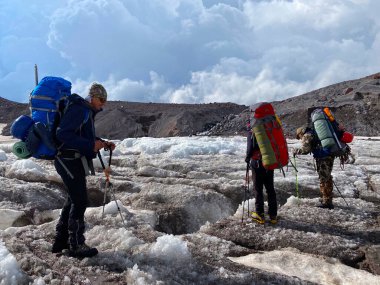 Sırt çantalı üç dağcı karlı bir dağ yolunda duruyor. Kuzey Elbrus bölgesinin güzel dağ manzarası.