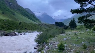 Akşam dağlarda. Fırtınalı dağ nehri. Kuzey Elbrus bölgesinin yeşil kayalık yamaçları. Güzel bir dağ manzaralı yaz manzarası.
