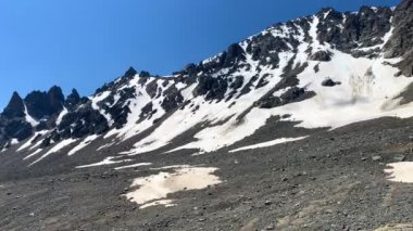 Tırmanışçı - bir gezgin kayalık bir dağda duruyor ve uzaklığa bakıyor. Güzel bir dağ kış manzarasının havadan görünüşü. Kuzey Elbrus bölgesinin kayalık yamaçları.