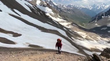 Büyük bir sırt çantası ve yürüyüş direkleri olan bir dağcı dağ yolunda yürüyor. Güzel bir dağ kış manzarasının havadan görünüşü. Kuzey Elbrus bölgesinin kayalık yamaçları.