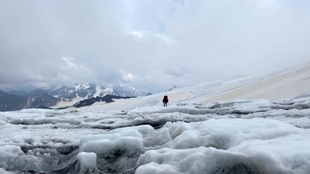 一个带着大背包和远足杆子的登山者沿着雪道走着 空中俯瞰美丽的高山冬季风景 Elbrus地区北部多雪的岩石斜坡 — 图库视频影像