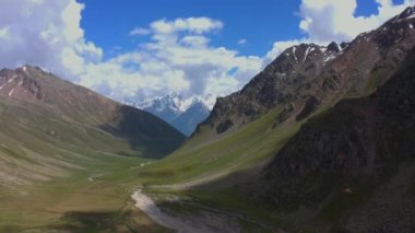 Güzel bir dağ kışı manzarasının üzerinde uçan bir kuşun hava görüntüsü. Kuzey Elbrus bölgesinin kayalık yamaçları. Beyaz bulutlu mavi gökyüzü.