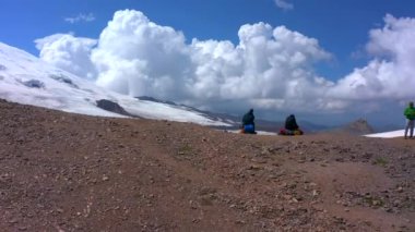 Sırt çantalı beş dağcı Elbrus Dağı 'nın önünde dinleniyor. Güzel bir dağ kış manzarasının havadan görünüşü. Kuzey Elbrus bölgesinde karla kaplı yamaçlar.