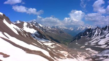 Güzel bir dağ kış manzarasının havadan görünüşü. Kuzey Elbrus bölgesinin kayalık yamaçları. Beyaz bulutlu mavi gökyüzü.