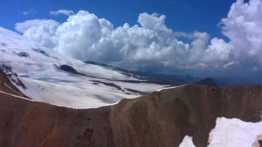 Güzel bir dağ kış manzarasının havadan görünüşü. Kuzey Elbrus bölgesinin kayalık yamaçları. Beyaz bulutlu mavi gökyüzü.