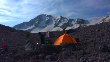 Elbrus Dağı 'nın önünde çadır kurmuşlar. Gezginler sırt çantalarını toplarlar. Kuzey Elbrus bölgesinin kayalık yamaçları. Dağ kış manzarası.