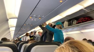 Aziz PETERSBURG, RUSSIA - 25 Ağustos 2020: bir hostes üst ranzada bir yolcu çantasına yardım eder. Koruyucu maskeli insanlar uçak kabinine giriyor..