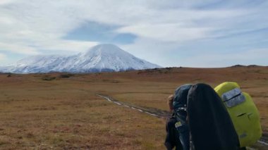Büyük sırt çantaları ve yürüyüş direkleri olan iki turist tundrada yol boyunca yürüyorlar. Klyuchevskoy volkan parkında gezinti. Sonbaharda Kamçatka Yarımadası 'na git..