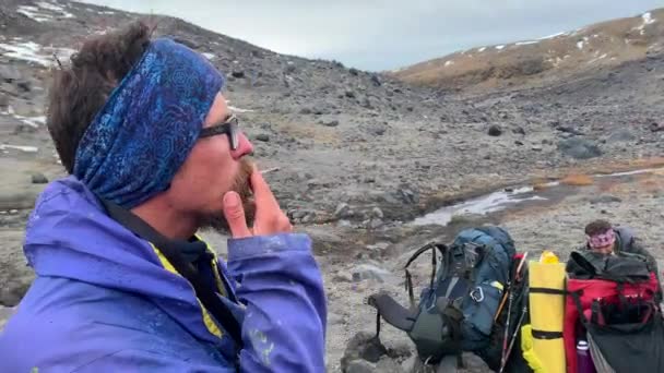 一个戴眼镜 头上戴着蓝色绷带的男人在休息时抽烟 在Klyuchevskoy火山公园旅行 前往堪察加半岛 — 图库视频影像