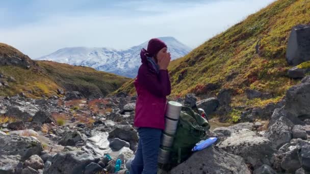 大きなリュックを背負った観光客の女の子が顔に太陽のクリームを塗り サングラスをかけている クリウチェフスキー火山公園でのトレッキング カムチャツカ半島への旅行 — ストック動画