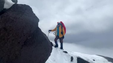 Büyük bir sırt çantası ve buz baltası ile karlı bir dağın tepesinde duran bir kaskla tırmanan. Dağ tırmanışı. Klyuchevskoy volkan parkında gezinti. Kamçatka Yarımadası 'na git..