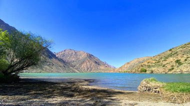 Güzel dağ gölü Iskanderkul sahilinde tatil. Arkasında tepeler, tepeler ve kayalar olan güzel bir gölet. Tacikistan 'a bir gezi. Huzur ve rahatlama