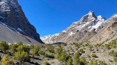 Alaudinsky gölleri vadisindeki karla kaplı kayalık vadi manzarası. Tacikistan, Asya 'ya git. Vahşi, el değmemiş bir bölge. İnce yeşil çalıları olan kayalık bir arazi.