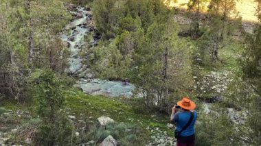 Kovboy şapkalı bir adam Tacikistan 'da bir dağ nehrinin fotoğrafını çekiyor. Seyahat, turizm ve özgürlük. Dokunulmamış vahşi yerler. Tacikistan 'daki Alaudin Gölleri Vadisi.