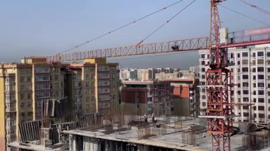 Şehirdeki yüksek katlı bir inşaat alanındaki vinç görüntüsü. Bir grup inşaat işçisi üst katta çalışıyor.