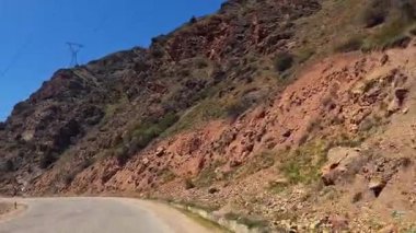 Kayalık bir vadi boyunca dolambaçlı bir yol. Yeşil yamaçlar, elektrik hatları ve karla kaplı dağlar. Tacikistan 'ın manzaralı yollarında bir araba yolculuğu.