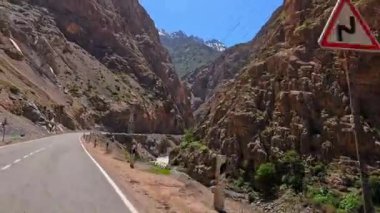 Fırtınalı bir dağ nehri boyunca bir araba sürüp kayalık bir uçurumdan geçmek. Elektrik hattı olan asfalt yol boyunca tuhaf yüksek dağ oluşumları..