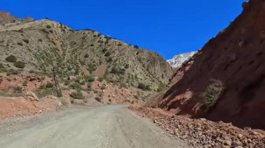 Tacikistan 'daki Iskanderkul Dağı Gölü' ne giden toprak bir yol. Karla kaplı dağ tepeleri, yeşil yamaçlar ve kırmızı kumlu kayalıklar. Maceralar ve yolculuklar