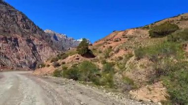 Tacikistan incisine giden toprak yolun manzarası - Iskanderkul Gölü. Dar, dolambaçlı bir yol kayalık bir dağ geçidinden geçiyor. Çevresindeki manzara inanılmaz.