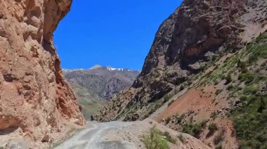 Tacikistan 'ın kayıp yerlerine arabayla gitmek. Vadinin içine uzanan toprak yolu olan kayalık bir dağ sırası. Yüksek uçurum ve yüksek iniş