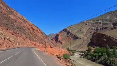 Kırmızı kayalar, dağ nehri ve yeşil uçurumlar boyunca asfalt yol boyunca bir araba yolculuğu. Yazın Tacikistan 'a bir gezi. Turizm ve macera. Özgürlük ve yolculuk